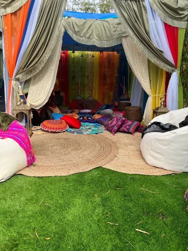Colorful outdoor tent with vibrant curtains and cushions, set on a carpeted grass area with bean bags around for a Dream Catcher Themed Party.
