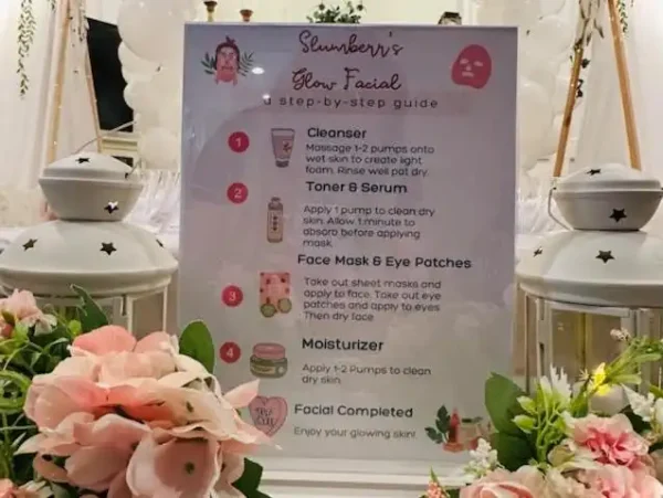 A sign for the "Spa Party with DIY Lip Gloss" at your spa event outlines five steps: Cleanser, Toner & Serum, Face Mask & Eye Patches, Moisturizer, and Facial Completed. The attractive display is adorned with flowers and candle lanterns. To add an extra touch of fun, participants can create their own DIY lip gloss!