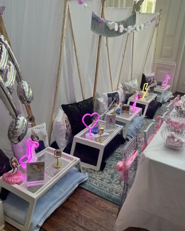 Create a Spa Party with DIY Lip Gloss featuring small wooden tables adorned with neon lights, cozy pillows, and chic decorations. Arrange the setup indoors against a white backdrop accented with balloon decorations. Treat your guests to a fun-filled experience as they create their own lip glosses.