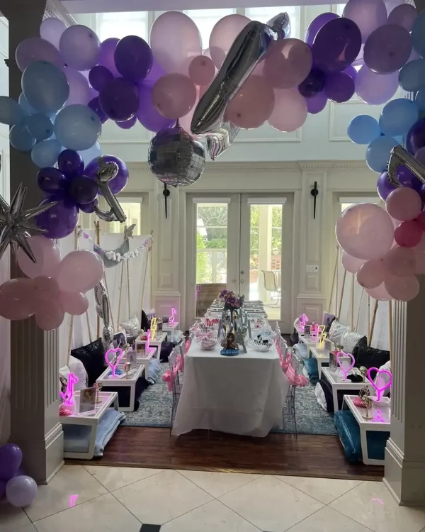 The "Spa Party with DIY Lip Gloss" transforms a room into a delightful children's spa setting with pink, purple, and blue balloons, a long dining table adorned with themed décor such as signs and miniature tents, and features an engaging DIY lip gloss station.