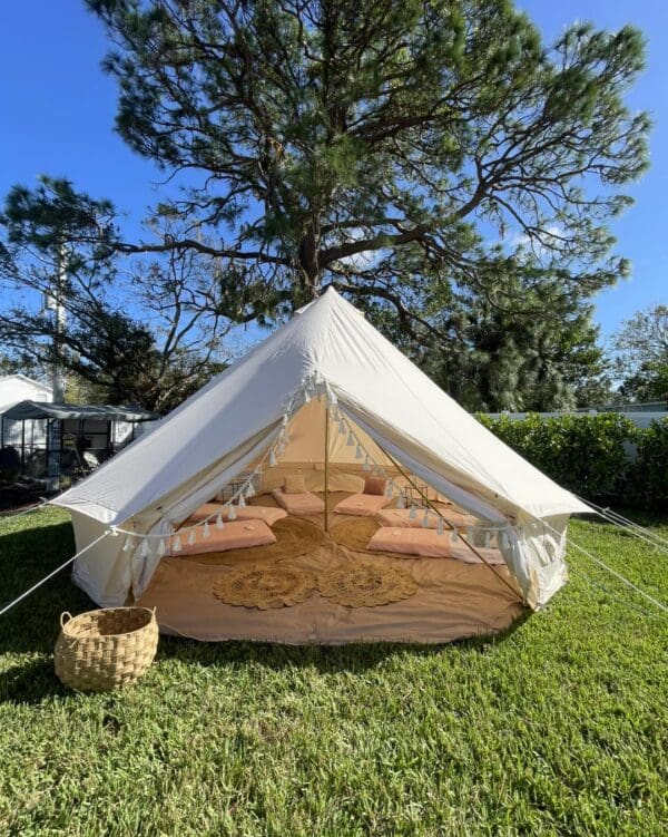 Capture the magic of the Movie Night Extravaganza under a sparkling, starry sky. This enchanting outdoor event boasts a picturesque white canvas tent elegantly pitched on vibrant, lush green grass. Just outside the tent, a charming picnic basket invites you to indulge in comfort and relaxation. Step inside to find an inviting ambiance where plush cushions and soft rugs create a cozy haven for an unforgettable cinematic experience. The serene scene is beautifully framed by the gentle presence of a nearby tree, enhancing this idyllic setting with natural charm. Perfect for those seeking unique outdoor entertainment in nature's embrace.