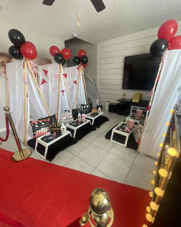 Experience an unforgettable Movie Night Extravaganza in a room transformed into a cinematic wonderland. Striking red and black balloons float above, paired with eye-catching striped banners that add to the festive atmosphere. Luxurious black and white seating invites you to relax and enjoy the show. Elevate your home theater experience with film-themed props meticulously placed throughout the space, creating an immersive setting perfectly designed for movie lovers.