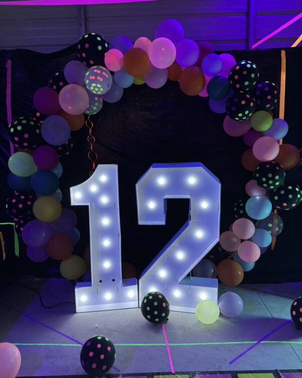 In the captivating setting of a Movie Night Extravaganza, a radiant illuminated number 12 takes center stage, surrounded by a stunning arch of colorful balloons adorned with playful polka dot patterns. This vibrant and festive display pops against the deep, dark background, perfectly capturing the essence of celebration and excitement. Ideal for events or parties seeking that cinematic magic and Instagram-worthy moments!