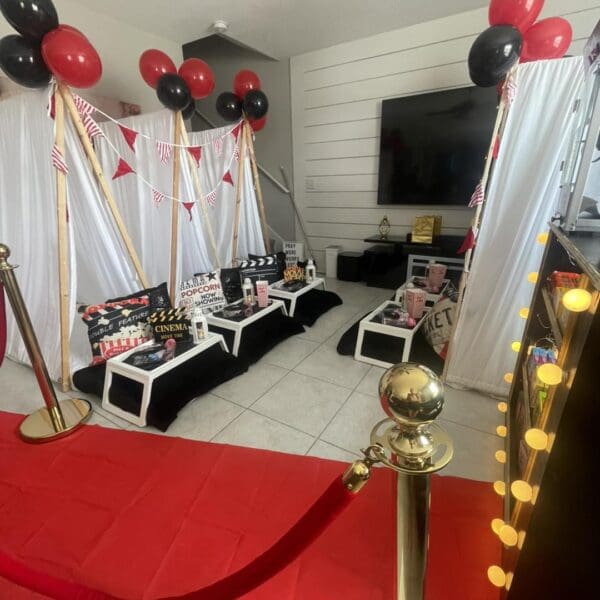 Get ready for an unforgettable Movie Night Extravaganza as this room transforms into a dazzling cinematic venue. Step onto the eye-catching red carpet, bordered by elegant gold stanchions that set the stage for a Hollywood-inspired evening. The decor radiates with vibrant black and red balloons, adding pops of color and style. Movie aficionados will appreciate the detailed movie-themed decor, featuring an iconic clapperboard and vintage film reels that seamlessly enhance the TV backdrop. This immersive setting captures the essence of a glamorous movie premiere night right at home!