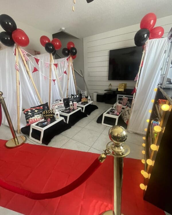 Get ready for an unforgettable Movie Night Extravaganza as this room transforms into a dazzling cinematic venue. Step onto the eye-catching red carpet, bordered by elegant gold stanchions that set the stage for a Hollywood-inspired evening. The decor radiates with vibrant black and red balloons, adding pops of color and style. Movie aficionados will appreciate the detailed movie-themed decor, featuring an iconic clapperboard and vintage film reels that seamlessly enhance the TV backdrop. This immersive setting captures the essence of a glamorous movie premiere night right at home!