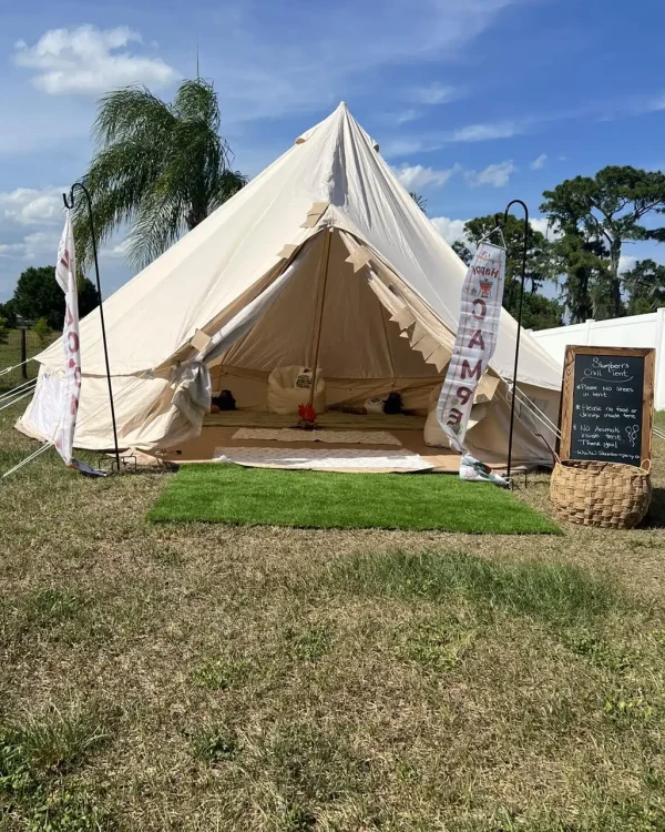 A large, white canvas tent is set up outdoors on a grassy area. Inside, the tent is furnished with cushions and a rug, perfect for a Harry Potter Themed Party. A chalkboard sign and decorative banner featuring Hogwarts motifs are placed nearby.