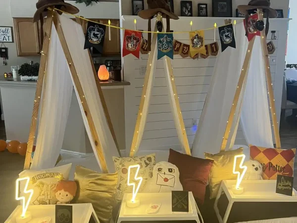 Three indoor tents decorated with Harry Potter-themed banners and pillows set the stage for a Harry Potter Themed Party. Each tent has a small table in front adorned with glowing lightning bolt lights and various Harry Potter items, creating an enchanting experience for fans of all ages.