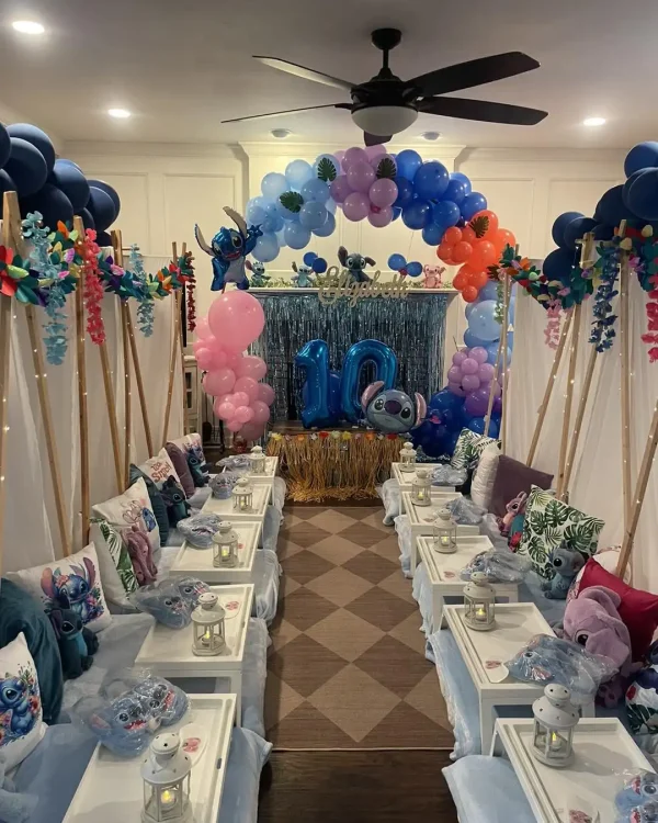 A decorated indoor space for a 10th birthday celebration with a blue and pink balloon arch, Harry Potter Themed Party decorations, and tables set up with plates, pillows, and small lanterns.