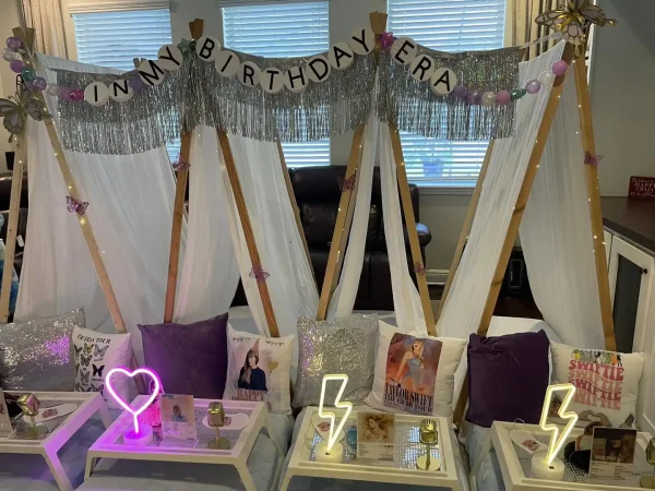 Three indoor tent setups with a "Taylor Swift Theme" banner above, capturing a Taylor Swift theme. The scene features purple pillows, books, and heart and lightning bolt decorations on small tables in front.