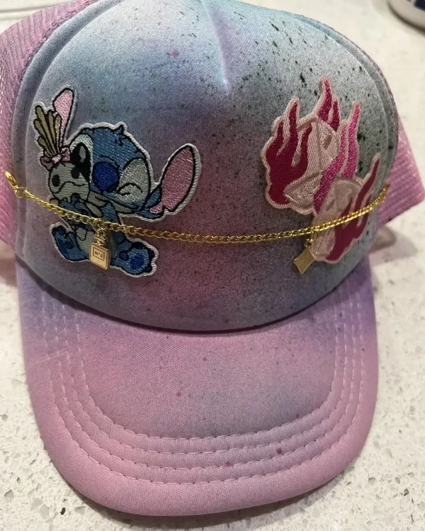 A hat from the Luxury Soft Play Packages sports a pink and purple gradient, featuring cartoon character and flame patches on the front, accented with a gold chain and small lock charm for an added touch of luxury.