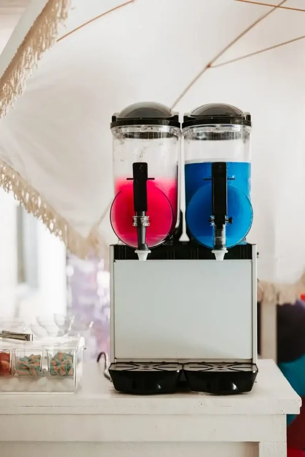 Our Event Photography Packages now feature a dual beverage dispenser, with a pink drink in the left chamber and a blue drink in the right chamber. Additionally, small containers filled with individually wrapped items on the left make it an ideal complement to our offerings.