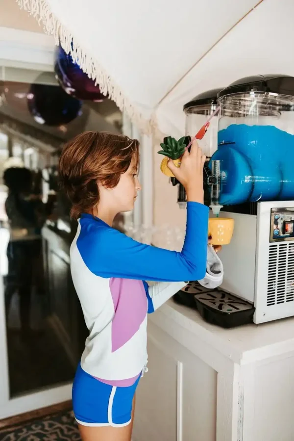 A young person in a blue and white swim shirt uses a slushie machine to fill a pineapple-shaped cup with blue slushie—an ideal moment captured by our Event Photography Packages.