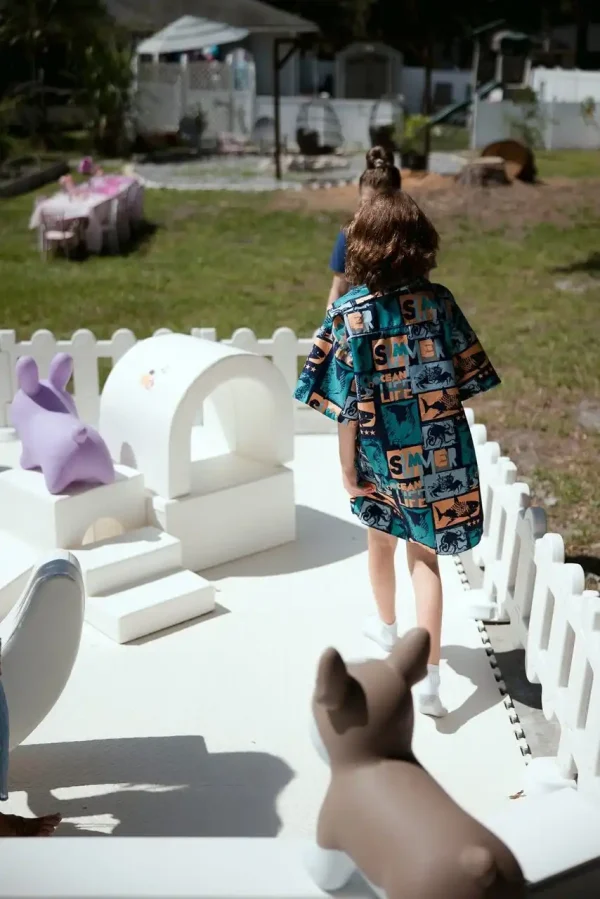 A child, dressed in a patterned frock, strolls along a white path bordered by white picket fences and an array of animal-shaped sculptures, creating an ideal scene for any Event Photography Packages.