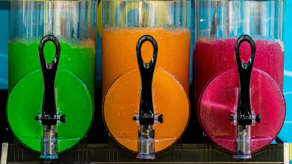 The Slushy/Margarita Bar Package includes three vibrant beverage dispensers filled with green, orange, and red drinks, likely margaritas or slushies, each featuring a black spout for convenient dispensing. Ideal for any bar setup.