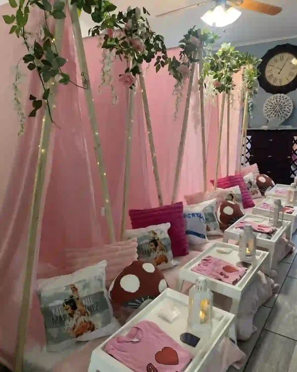 Experience the ultimate cozy indoor sleepover with a stunning setup that promises comfort and style. Picture this: pink teepee tents adorned with lush green foliage, surrounded by plush polka dot pillows to create a whimsical yet luxurious ambiance. At the heart of this chic scene is a refined ensemble from Adult Ghost Chairs & Table Rentals, seamlessly blending elegance with modern flair. A candle lantern, artfully placed on a tray table, casts a warm glow over the entire setting. Soft pink bedding adds layers of comfort while ceiling lights illuminate the scene in gentle tones. A large wall clock serves as an elegant focal point, tying together the inviting atmosphere of this dream-worthy sleepover sanctuary. Perfect for intimate gatherings or memorable slumber parties!