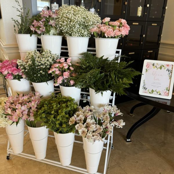 A captivating flower cart brimming with elegance showcases a stunning floral display, featuring white ceramic vases overflowing with delicate pink and white blooms. The arrangement includes enchanting pink roses and airy sprigs of baby's breath, artfully presented on a sophisticated multi-tiered metal stand. A charming decorative sign nearby invites passersby with the words "Flowers for You," adding an inviting touch to the scene. In the background, a sleek black cabinet with multiple compartments complements the vibrant floral ensemble, offering an enticing backdrop to this picturesque flower display. Perfect for anyone seeking inspiration in floral arrangements or lovers of exquisite nature-themed decor!