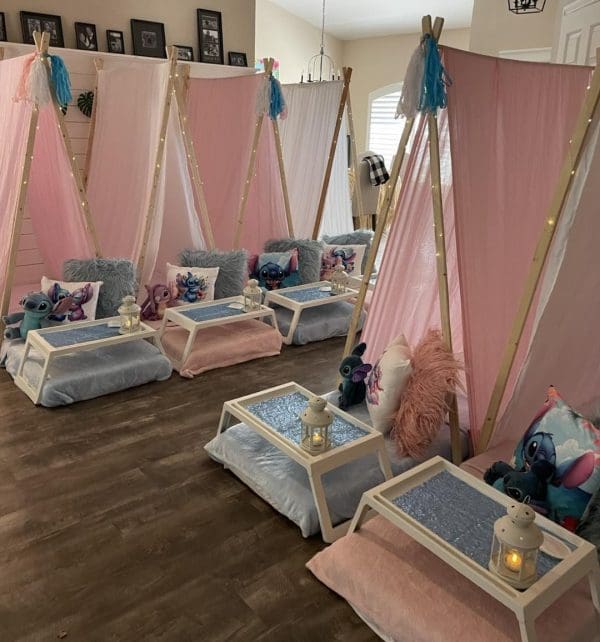 Get ready for the ultimate kids' sleepover experience in 2024 with this enchanting setup! This cozy and inviting scene features an array of charming small tents crafted from pink and white fabric, each thoughtfully equipped with a plush cushion, a snuggly soft blanket, and a petite table perfect for midnight snacks or delightful activities. Adding to the magical ambiance are adorable plush toys and whimsical lanterns scattered throughout the space. Twinkling fairy lights cast a warm glow, creating an inviting atmosphere that promises unforgettable memories. The rustic wooden floor enhances the homey feel of this stylish setup, while framed photos adorning the wall showcase creative sleepover themes to inspire endless fun. Ideal for fostering imagination and adventure, this well-curated environment is perfect for hosting dreamy children's slumber parties in style!