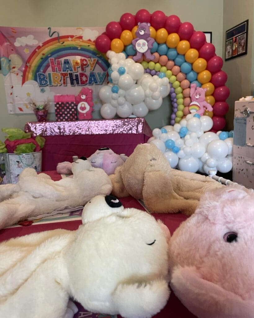 Vibrant birthday celebration scene featuring an eye-catching arch of colorful balloons that adds a pop of excitement to the ambiance. A cheerful "Happy Birthday" banner stretches across the room, setting a festive tone. The focal point is a charming display on the table adorned with an array of adorable plush toys, creating a playful atmosphere perfect for capturing joyful memories at this unforgettable birthday bash. Perfect backdrop for children's party photos or joyful event content!