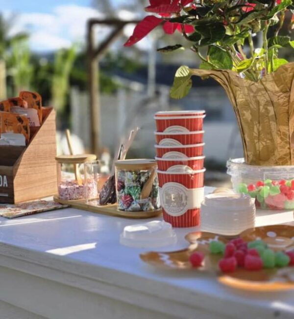 Create the perfect outdoor coffee setup with our vibrant arrangement featuring stacked red coffee cups, a rustic wooden box brimming with delicious snacks, and jars of colorful candy. Nestled next to these delights is a decorative green plant on a pristine white table, setting the stage for an inviting gathering. Elevate the experience further by renting our Snow Machine to sprinkle some wintry magic over your event, transforming it into an enchanting winter wonderland that captivates all attendees. Ideal for outdoor gatherings and cozy winter-inspired events!