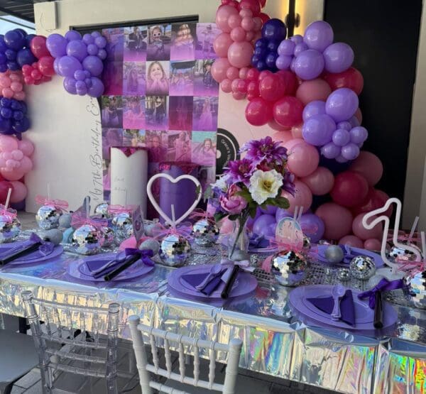 Celebrate in style with a captivating birthday party setup featuring a vibrant purple and pink theme. Discover the enchanting atmosphere created by colorful balloons floating above, complemented by an eye-catching collage backdrop that sets the perfect scene for memorable photos. Add a touch of glamour with dazzling disco ball centerpieces that catch the light and create mesmerizing reflections. Elevate your dining experience with elegant purple plates resting on an iridescent tablecloth, adding a subtle shimmer to every bite. The highlight of this cinematic-inspired celebration is the Movie Concession Stand Rental, bringing a unique Hollywood twist to your special day. Perfect for movie lovers and those seeking an unforgettable birthday experience, this party setup combines creativity and entertainment in equal measure.