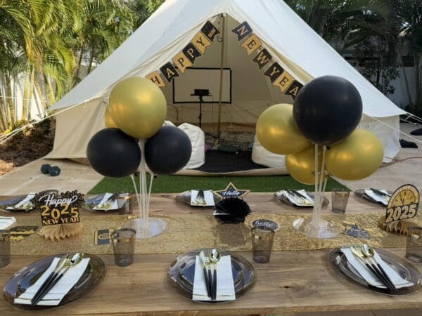 Celebrate the arrival of 2025 in style with an enchanting New Year's Eve setup! Under a spacious tent, vibrant black and gold balloons add a touch of elegance and festivity. The centerpiece—an exquisitely decorated table—boasts "Happy New Year" banners, perfectly capturing the spirit of new beginnings. Adding an extra layer of entertainment to your celebration is a Movie Concession Stand Rental, providing endless fun for guests of all ages. This captivating display promises to make your New Year’s Eve party both memorable and unforgettable! Ideal for those searching for unique themed party ideas or eye-catching New Year’s decor inspiration.