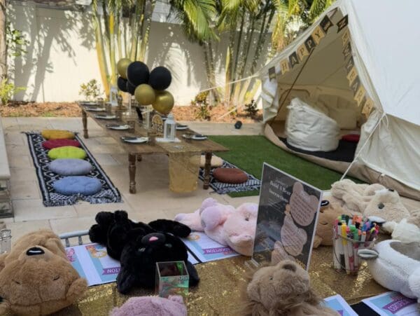 Experience the ultimate outdoor birthday party extravaganza with a stunning setup designed to captivate and delight. A beautifully laid-out long table adorned with plush cushions invites guests to relax and enjoy the festivities, while elegant black and gold balloons float above, adding a touch of sophistication. The centerpiece—a striking "Happy Birthday" tent—perfectly captures the celebratory spirit. Surrounding this enchanting scene are adorable stuffed animals and vibrant craft supplies that spark creativity and fun for all ages. The highlight of the event is undoubtedly the charming Movie Concession Stand Rental, serving freshly popped popcorn and an array of delightful treats, enhancing the festive atmosphere with nostalgic charm. Perfect for those searching for unique birthday party ideas or outdoor event inspirations.