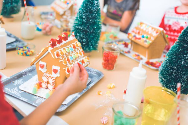 A group of joyful children enthusiastically decorating gingerbread houses at a vibrant holiday crafting table, complete with colorful candies and creamy frosting. The scene is beautifully set amidst an enchanting forest of miniature pine trees and cheerful festive decorations, capturing the essence of holiday fun and creativity. Perfect for Christmas-themed activities, family bonding, and holiday culinary crafts.