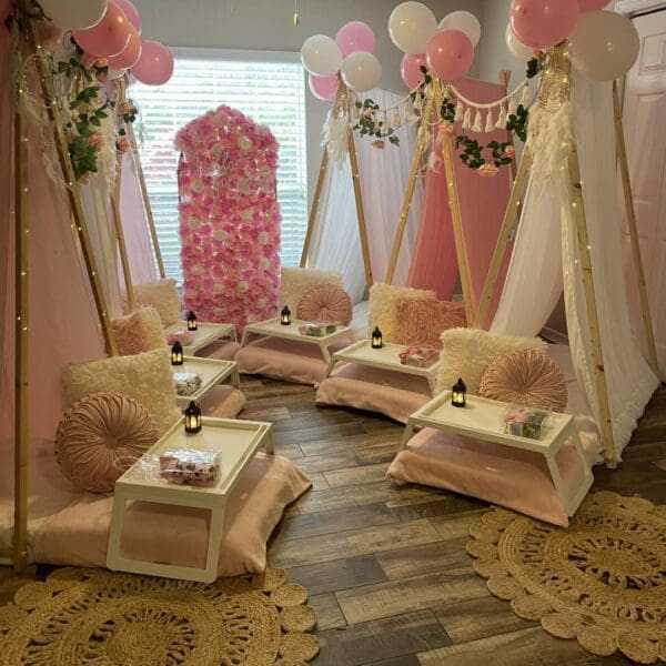 Capture the ultimate sleepover experience with a cozy room featuring four beautifully decorated tents, each exuding charm and whimsy. The enchanting scene is adorned with vibrant pink and white balloons floating above, perfectly complementing an exquisite flower wall that serves as a stunning backdrop. Small tables are strategically placed near each tent, inviting guests to indulge in snacks and games. Plush decorative rugs cover the polished wooden floor, adding warmth and comfort to the ambiance. To elevate this magical gathering, an outdoor projector beams exciting movies onto a huge inflatable screen, promising an unforgettable night under the stars filled with laughter and cinematic adventure. Perfect for creating lasting memories in style!.