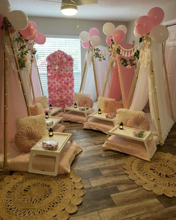 Capture the ultimate sleepover experience with a cozy room featuring four beautifully decorated tents, each exuding charm and whimsy. The enchanting scene is adorned with vibrant pink and white balloons floating above, perfectly complementing an exquisite flower wall that serves as a stunning backdrop. Small tables are strategically placed near each tent, inviting guests to indulge in snacks and games. Plush decorative rugs cover the polished wooden floor, adding warmth and comfort to the ambiance. To elevate this magical gathering, an outdoor projector beams exciting movies onto a huge inflatable screen, promising an unforgettable night under the stars filled with laughter and cinematic adventure. Perfect for creating lasting memories in style!.