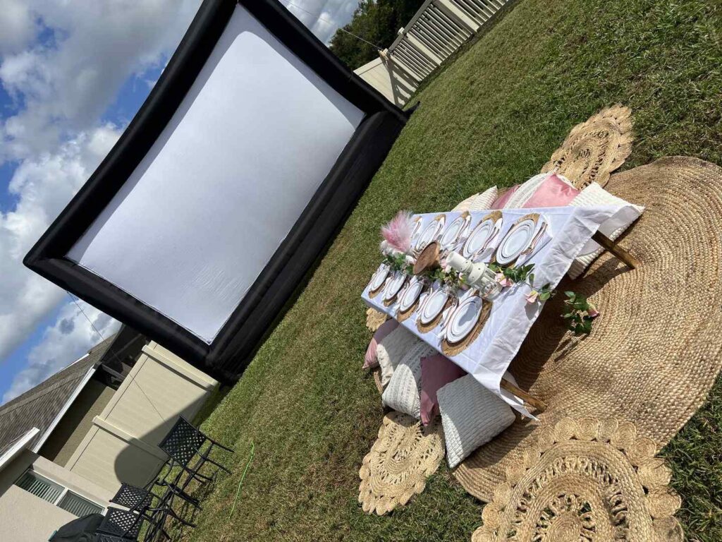 Celebrate Mom with an outdoor Mother’s Day lounge party featuring an inflatable movie screen, a low table set for dining, and cozy cushions on woven mats for the perfect grass-side gathering.